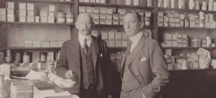 Aged photograph of gentlemen standing in front of tea stock in a shop.